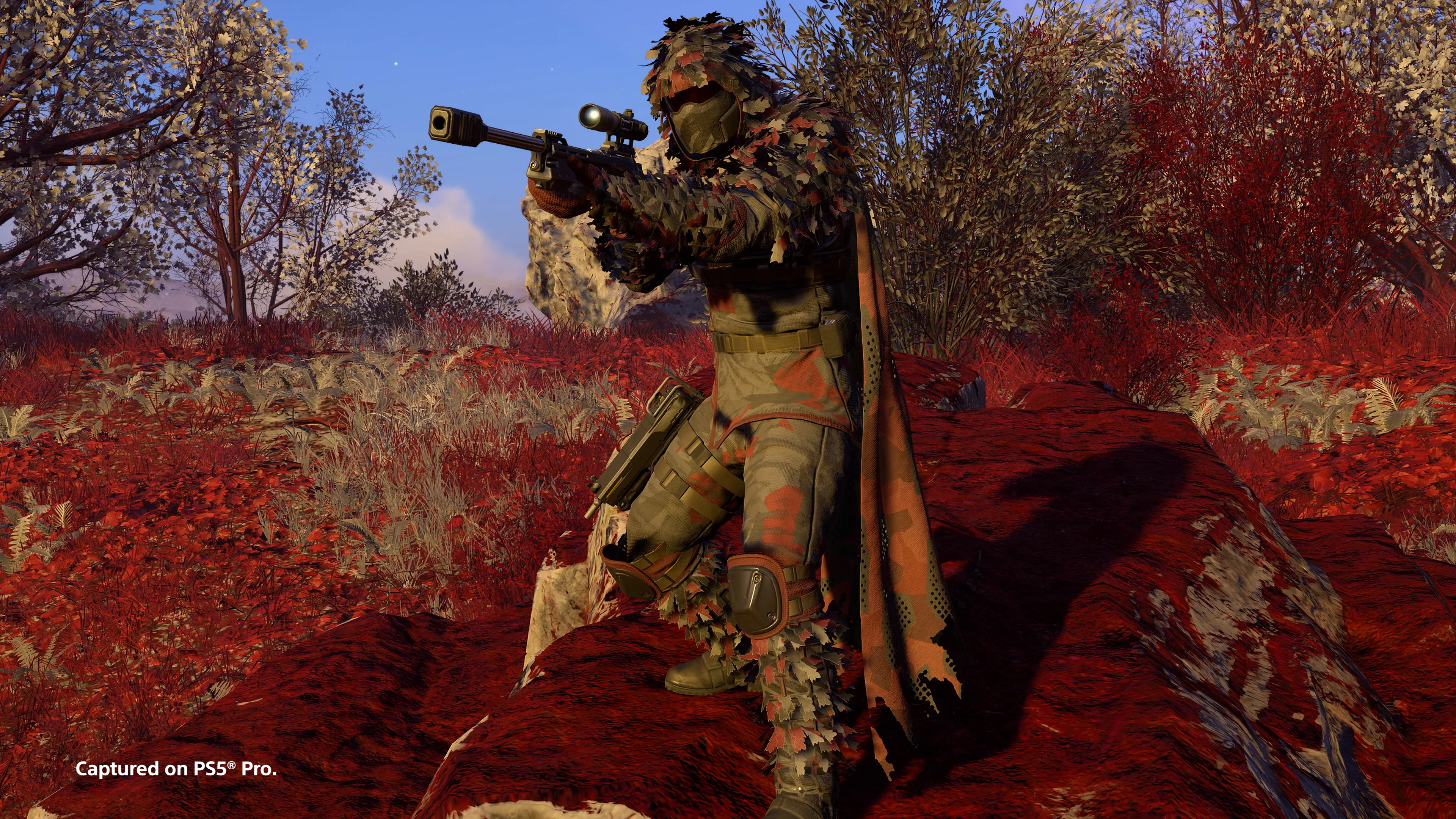 Helldiver en tenue de camouflage feuillue visant dans une forêt aux couleurs rouges.
