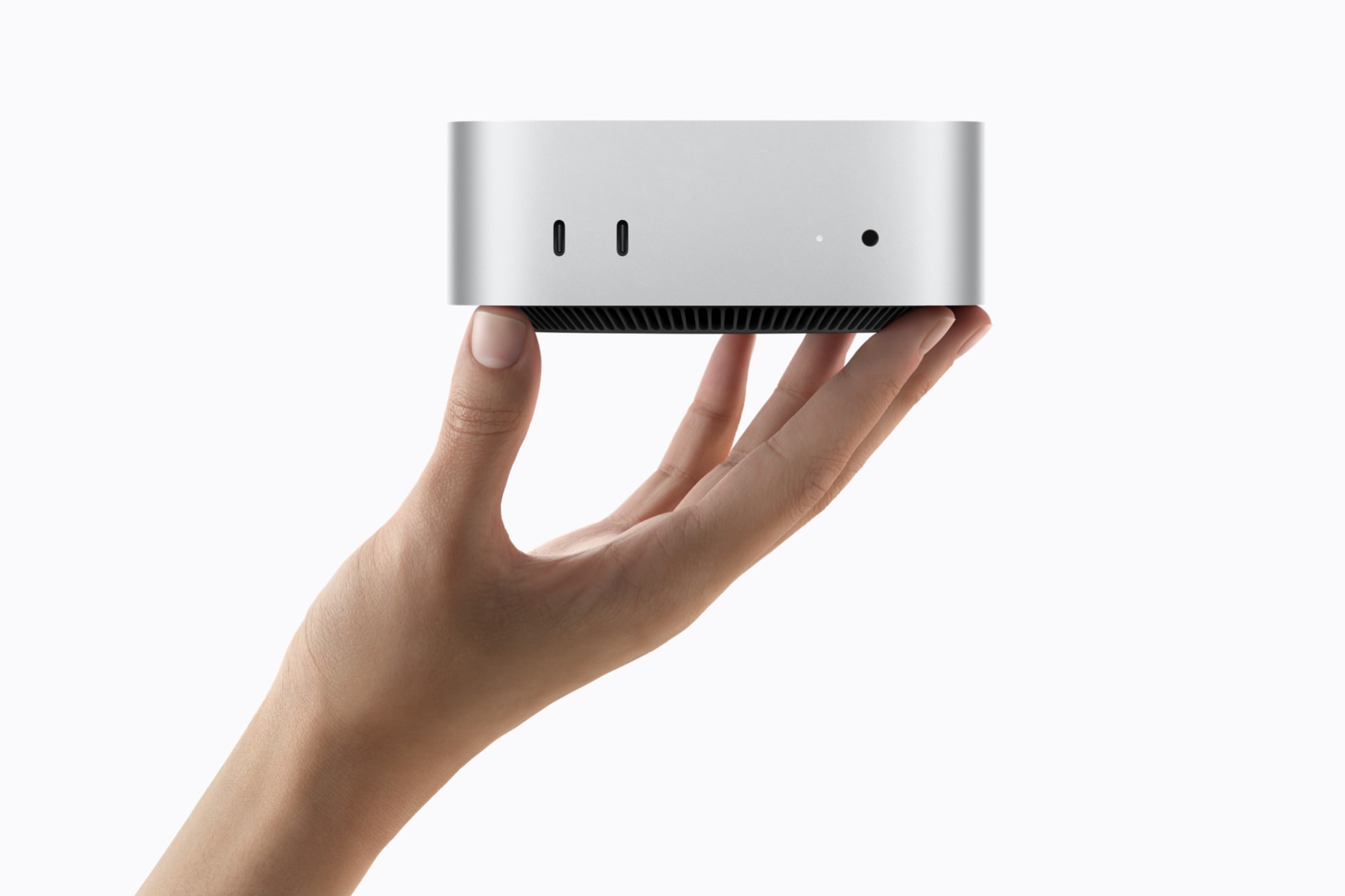 Photographie officielle du Mac mini M6 tenu dans une main, avec ses deux ports USB-C et sa prise casque en façade.