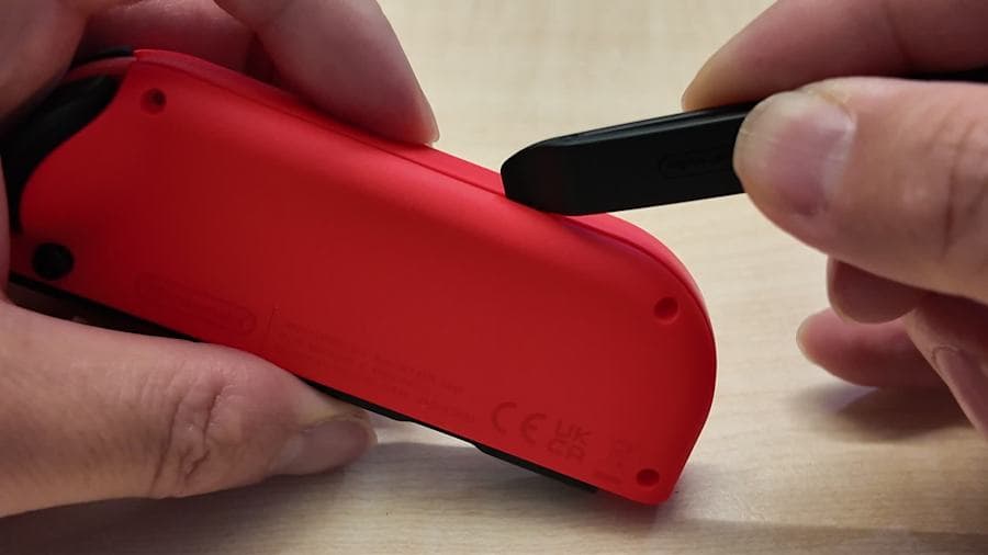 Ouverture d’un Joy-Con rouge révisé avec un outil en plastique dans le guide vidéo officiel Nintendo.