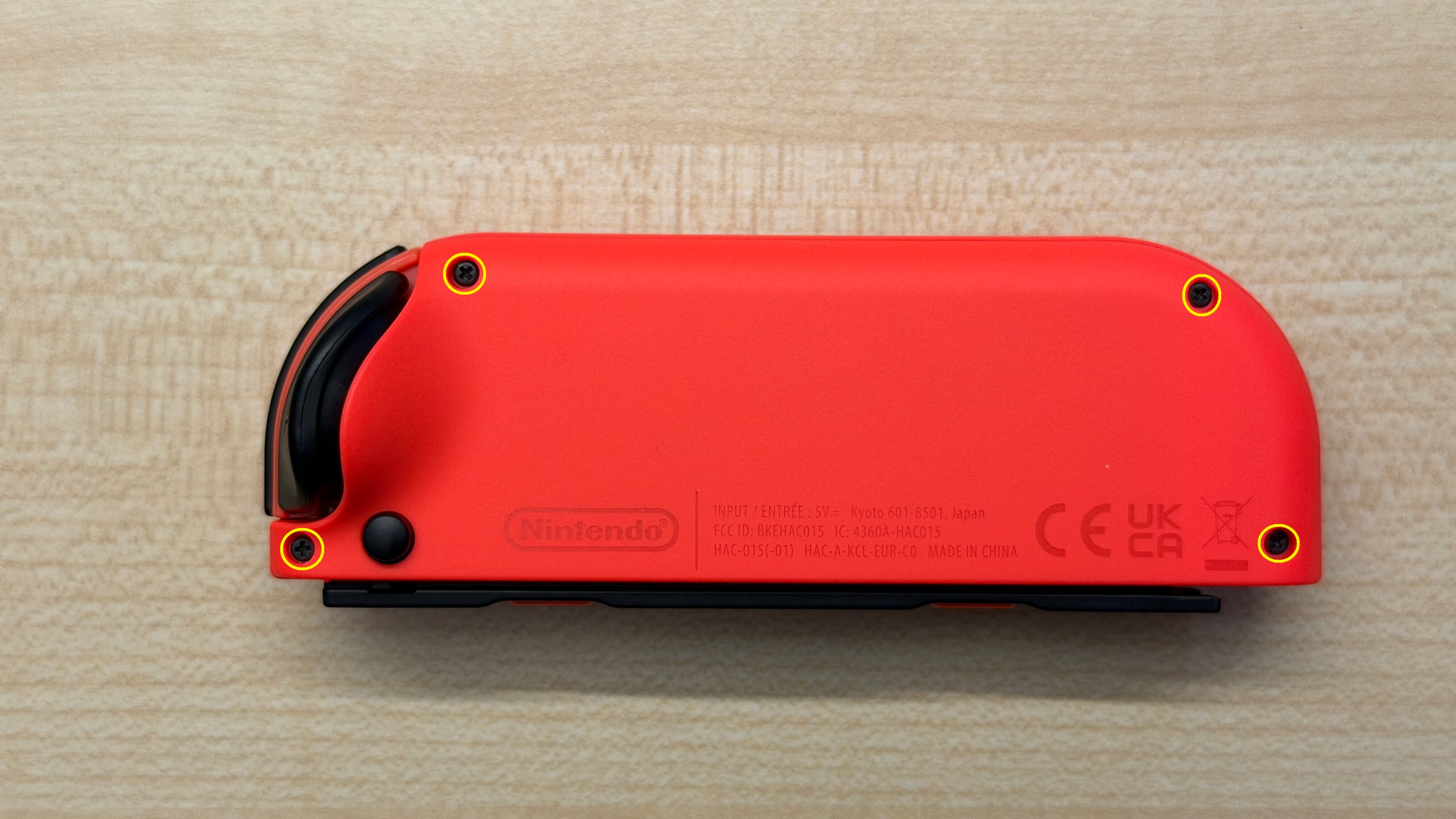Dos d’un Joy-Con rouge révisé avec ses quatre vis cruciformes entourées par Nintendo.
