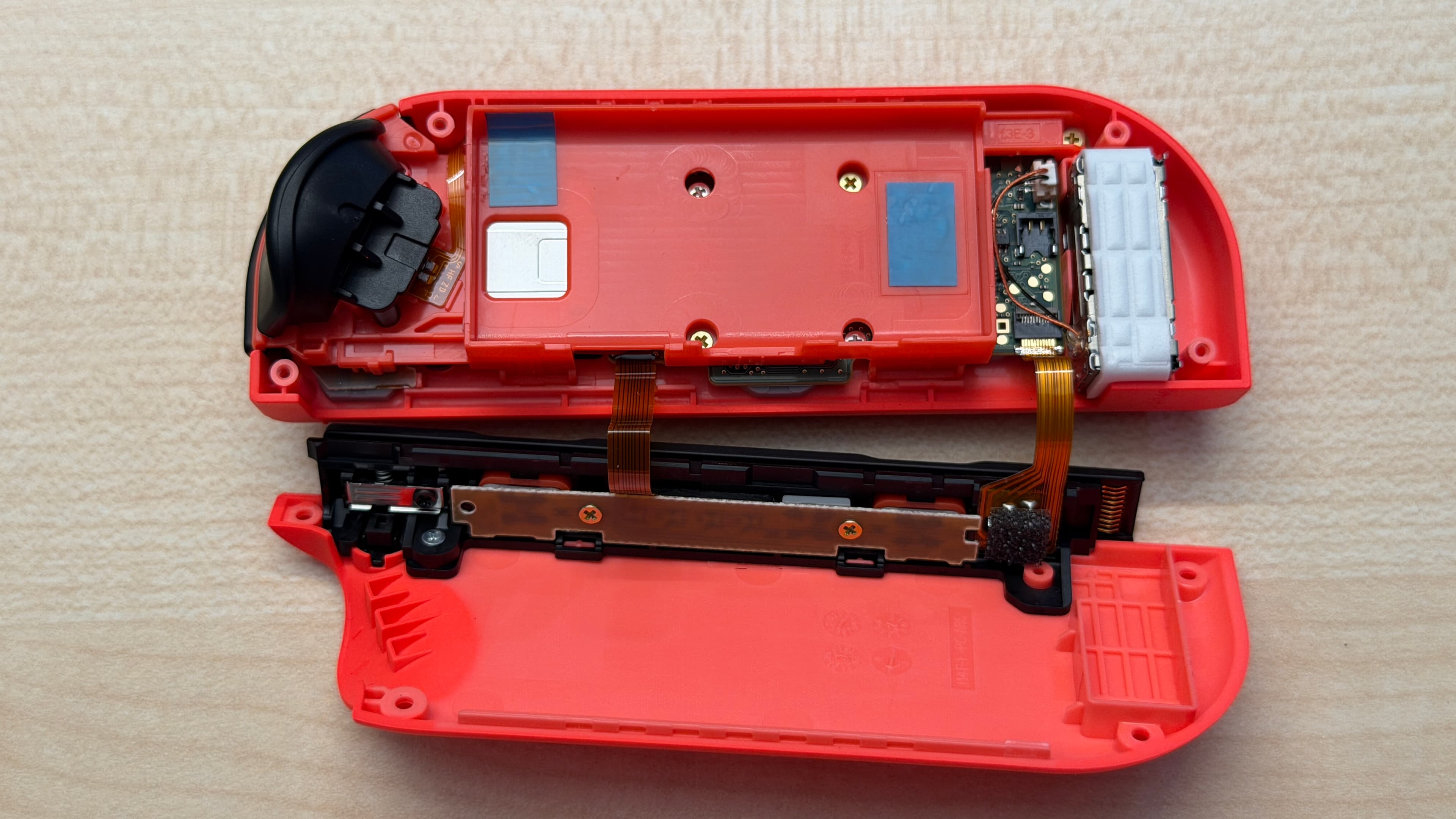 Intérieur d’un Joy-Con gauche avec les nouvelles bandes adhésives de fixation de batterie indiquées en bleu.