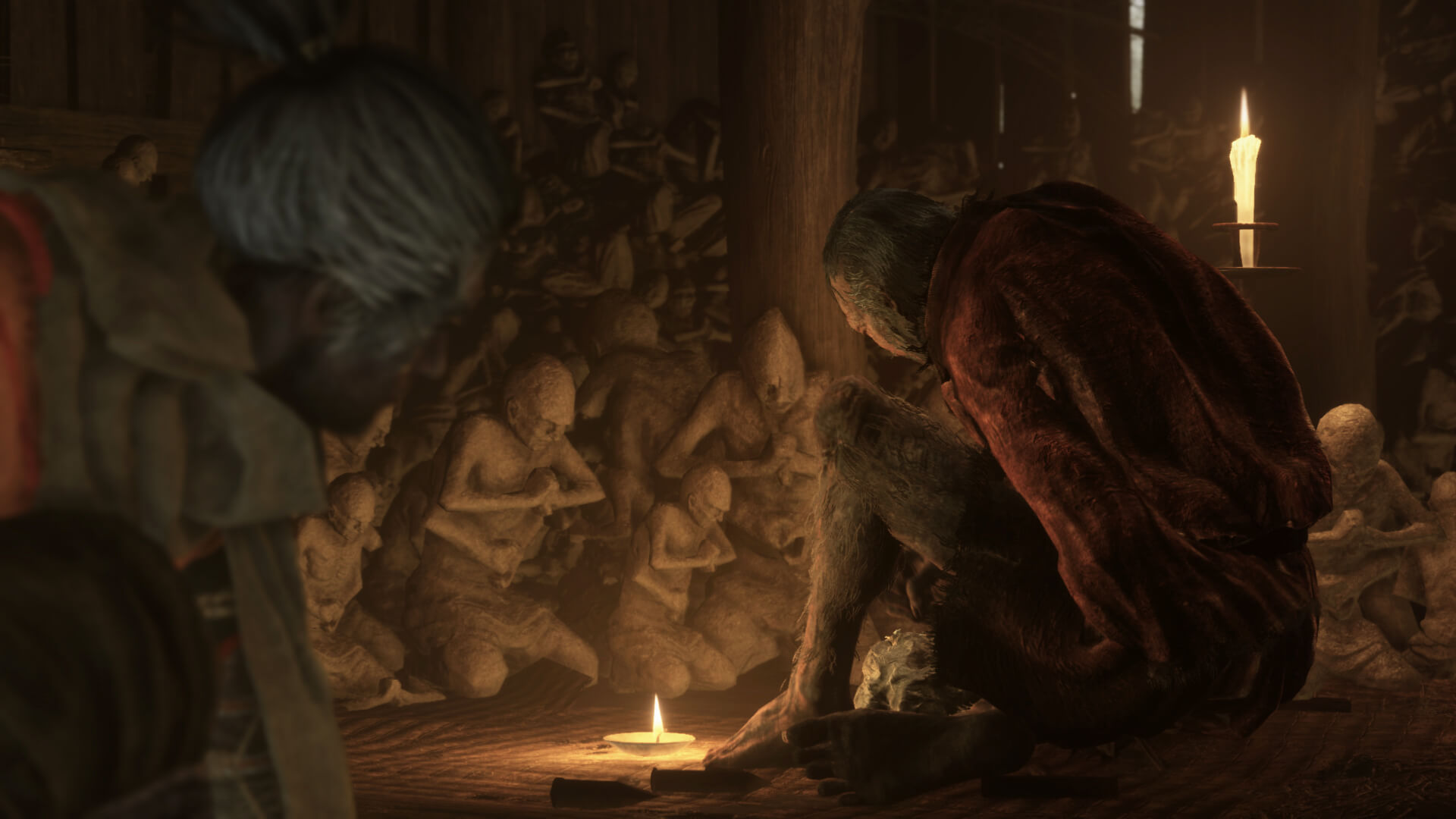 Un personnage âgé se tient auprès de statues et d’une bougie.